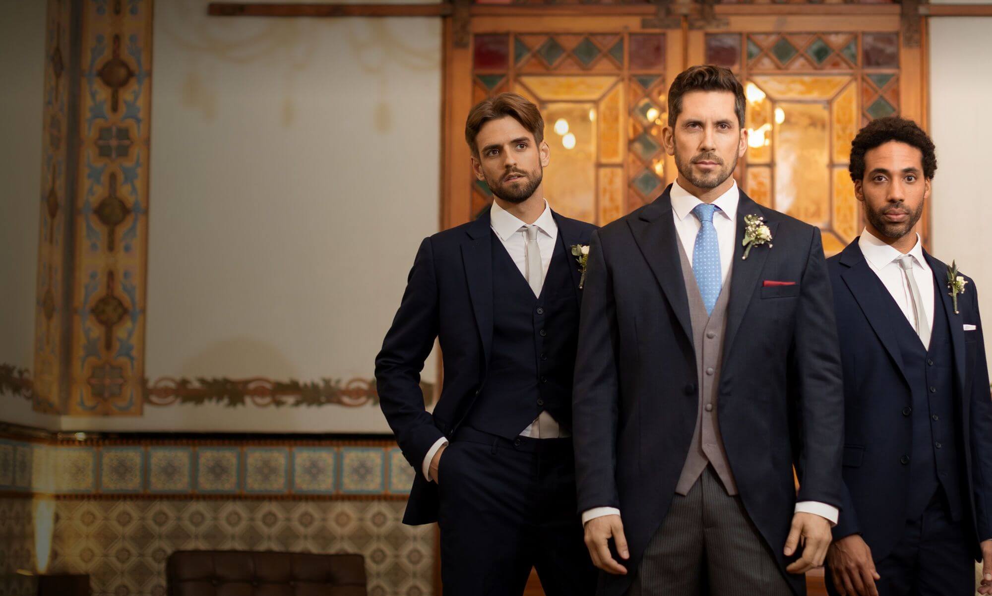 Three men wearing custom wedding suits in a classic indoor setting, showcasing tailored fit and elegant groom style.